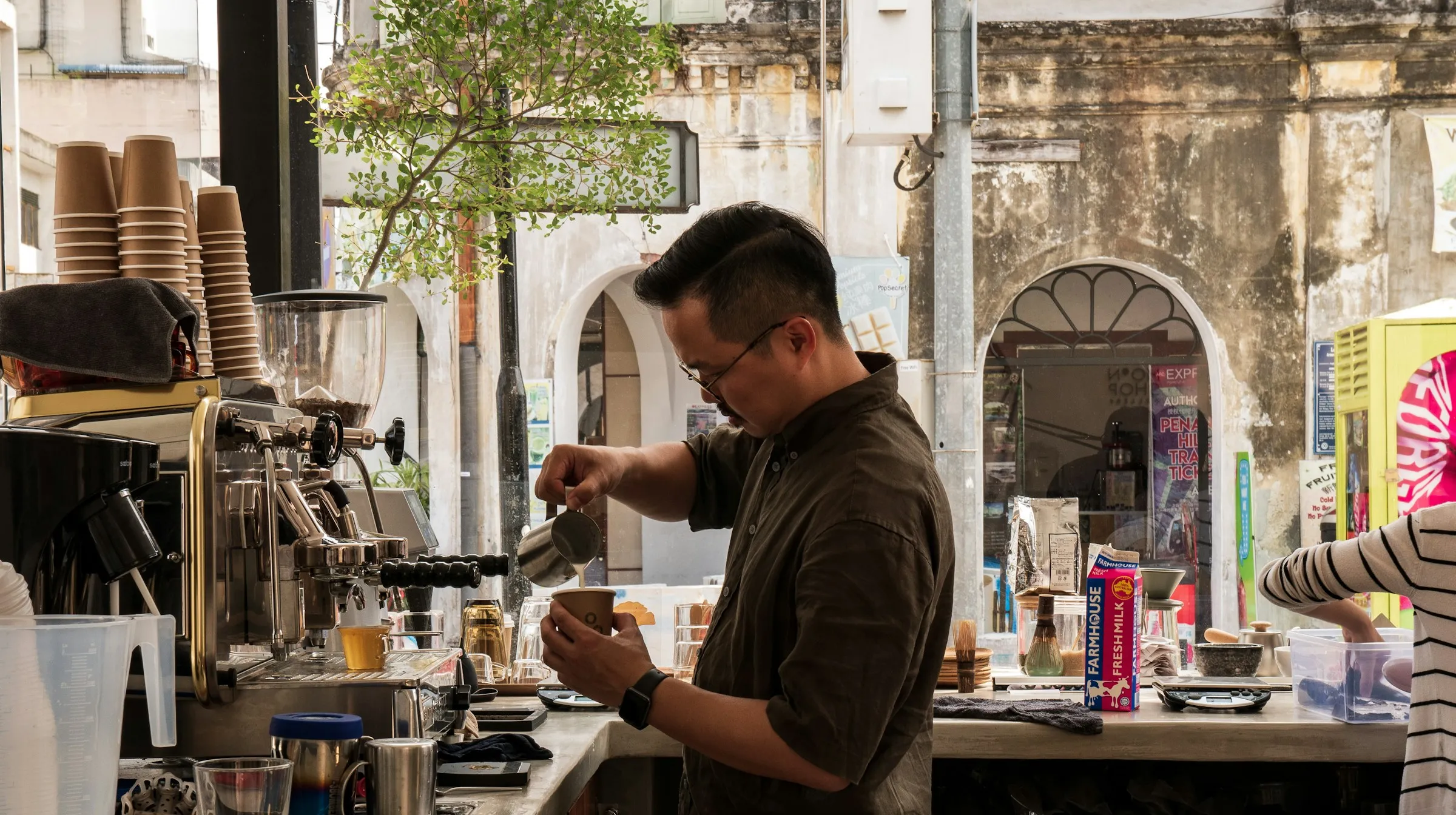 A barista pouring steamed milk in a busy café.