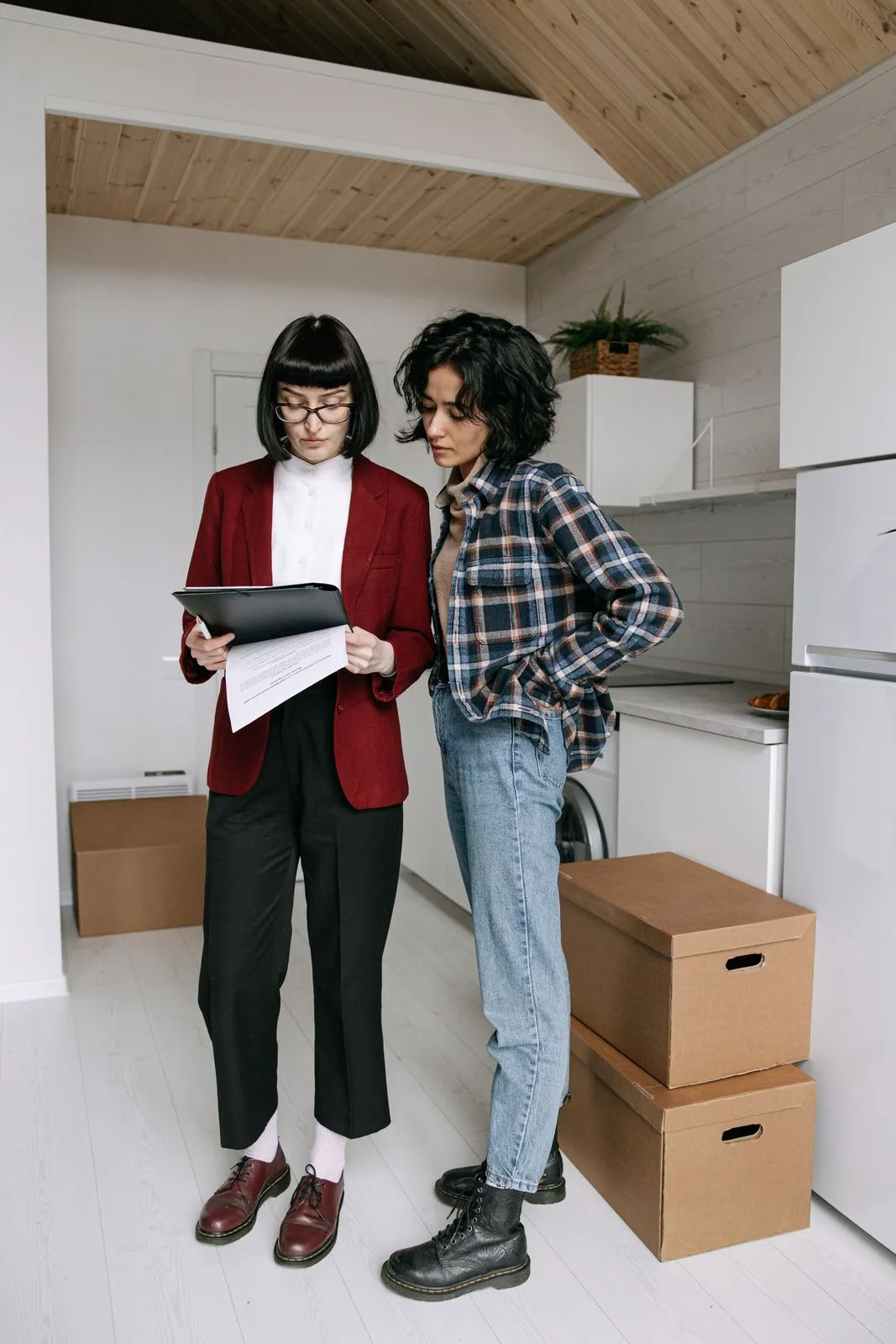 A property manager with a clipboard talking to a tenant in a kitchen full of moving boxes.
